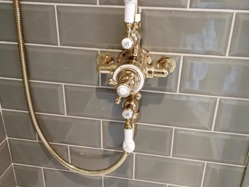 Close-up of brass shower controls on a tiled bathroom wall